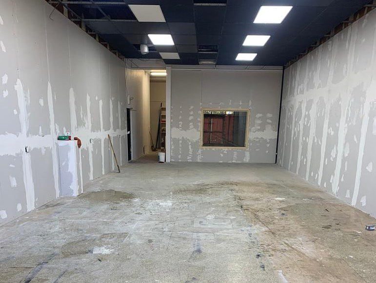 The interior of a commercial unit during construction, showing a newly installed drop ceiling with recessed lighting and a partition wall with a pass-through window.