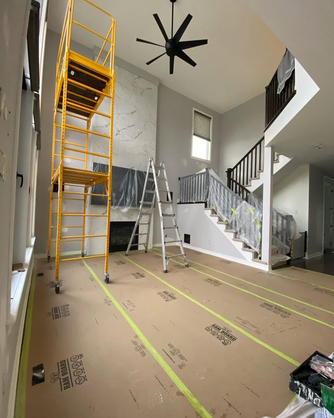 A professional Ottawa Painting Company. Interior residential space under renovation, with floors protected by Ram Board, a fireplace with a large marble-effect surround, and a staircase covered in plastic for protection.