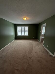Empty residential bedroom with dark green walls and beige carpet before professional repainting.