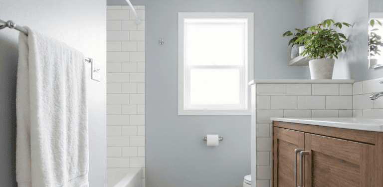 A modern bathroom showing a wood vanity, white subway tile, a potted plant on a shelf, and a white towel on a rack.